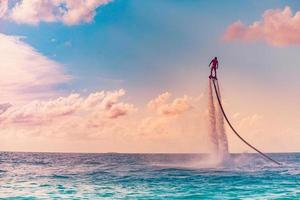 Maldives island sunset. Professional fly board rider doing back flip with tropical resort island background. Sunset sport and summer activity background, fun water sport photo