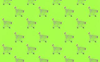 Shopping addiction, shopping lover or shopaholic concept. Many small empty shopping carts perform a pattern on a pastel colored paper background. Flat lay composition, top view photo