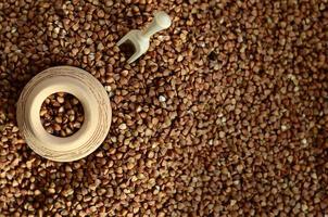 Background image of a large pile of buckwheat, in the middle of which lies a small jug and a wooden spatula for cereals photo