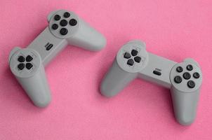 Playing games concept. Two pad joysticks lies on the blanket of furry pink fleece fabric. Controllers for video games on a background texture of light pink soft plush fleece material photo