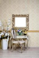 A fragment of a retro interior with a chair and table, on which is a telephone and a vase of flowers. Above the table hangs an empty picture frame for your photo