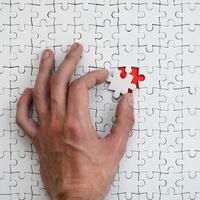 The texture of a white puzzle puzzle in the assembled state with one missing element that the male hand puts in photo