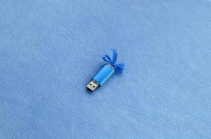 la tarjeta de memoria flash usb azul brillante con un lazo azul se encuentra sobre una manta de tela de vellón azul claro suave y peluda. diseño clásico de regalo femenino para una tarjeta de memoria foto