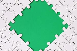 Framing in the form of a rhombus, made of a white jigsaw puzzle around the green space photo