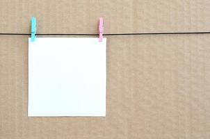 White blank card on rope on a brown cardboard background. Creative reminder, small sheet of paper on wooden clothespin, memo backdrop photo