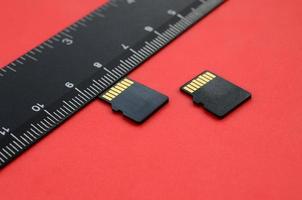 Two small micro SD memory cards lie on a red background next to a black ruler. A small and compact data and information store photo