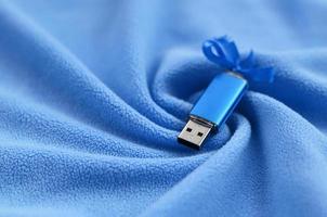 Brilliant blue usb flash memory card with a blue bow lies on a blanket of soft and furry light blue fleece fabric with a lot of relief folds. Memory storage device in women's design photo