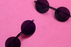 dos elegantes gafas de sol negras con gafas redondas se encuentran sobre una manta hecha de suave y esponjosa tela de lana rosa claro. imagen de fondo de moda en colores femeninos foto