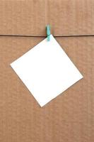 White blank card on rope on a brown cardboard background. Creative reminder, small sheet of paper on wooden clothespin, memo backdrop photo