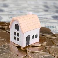 Mini house model on big coins stack on many dollar bills as background photo