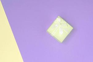 una pequeña caja de regalo amarilla se encuentra en el fondo de textura de los colores amarillo pastel y violeta de la moda foto