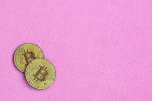 Two golden bitcoins lies on a blanket made of soft and fluffy light pink fleece fabric. Physical visualization of virtual crypto currency photo