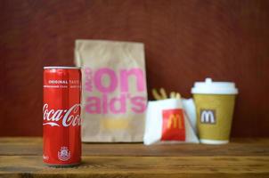 KHARKOV, UKRAINE - DECEMBER 9, 2020 McDonald's take away paper bag and french fries with coca cola can on wooden table photo