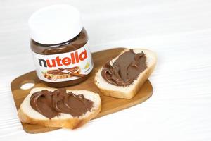 kharkov, ucrania - 27 de diciembre de 2020 lata de vidrio de nutella y untada en pan recién horneado. nutella es fabricada por la empresa italiana ferrero introducida por primera vez en 1964 foto