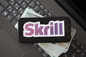 TERNOPIL, UKRAINE - SEPTEMBER 6, 2022 Skrill paper logotype lies on black laptop with US dollar bills. Payoneer is American financial services company provides online money transfer photo