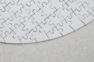A white jigsaw puzzle in the complete form lies on a treated stone surface. Textured image with copy space photo