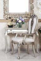 A fragment of a retro interior with a chair and table, on which is a telephone and a vase of flowers. Above the table hangs an empty picture frame for your photo