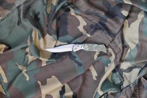 Military knife on army camouflage clothes close up. Background with copy space for military or special service design photo