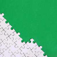 Fragment of a folded white jigsaw puzzle on the background of a green plastic surface. Texture photo with copy space for text