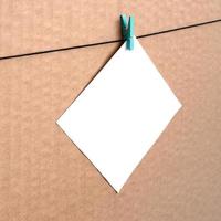 White blank card on rope on a brown cardboard background. Creative reminder, small sheet of paper on wooden clothespin, memo backdrop photo