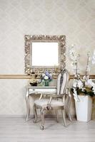 A fragment of a retro interior with a chair and table, on which is a telephone and a vase of flowers. Above the table hangs an empty picture frame for your photo