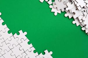 Fragment of a folded white jigsaw puzzle and a pile of uncombed puzzle elements against the background of a green surface. Texture photo with space for text