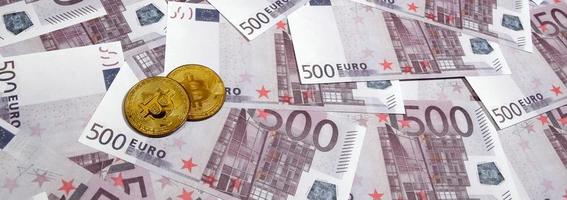 Bitcoins over pile of five hundred euro banknotes. Traditional money versus cryptocurrency concept. Gold coin above 500 euro bills. Close up photo