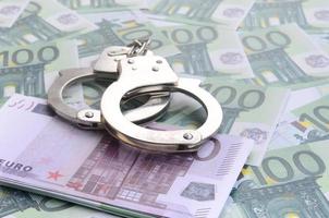 Police handcuffs lies on a set of green monetary denominations of 100 euros. A lot of money forms an infinite heap photo