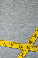 Yellow measuring tape lies on a gray knitted fabric photo