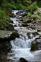 Close-up image of a small wild waterfall in the form of short streams of water between mountain stones photo