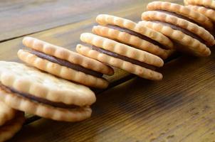 A round sandwich cookie with coconut filling lies in large quantities on a brown wooden surface. Photo of edible treats on a wooden background with copy space