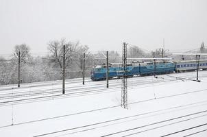 A long train of passenger cars is moving along the railway track. Railway landscape in winter after snowfall photo