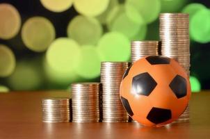 Soccer ball and stacks of golden coins in growth graph on the blurred bokeh background photo