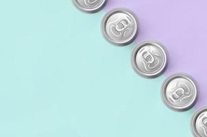 muchas latas de cerveza metálicas sobre fondo de textura de papel de colores violeta pastel y azul de moda en concepto mínimo foto