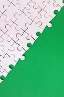 Fragment of a folded white jigsaw puzzle on the background of a green plastic surface. Texture photo with copy space for text