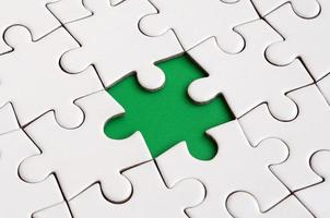 Close-up texture of a white jigsaw puzzle in assembled state with missing elements forming a green pad for text. Copy space photo