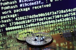 Two bitcoins lies on a videocard surface with background of screen display of cryptocurrency mining by using the GPUs photo