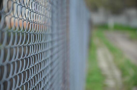A photograph of a metal net used as a fence of private possessions. Old metal grid in perspective with a blurred background photo