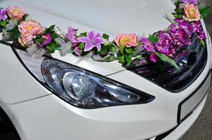una foto detallada del capó del coche de la boda, decorado con muchas flores diferentes. el coche está preparado para una ceremonia de boda