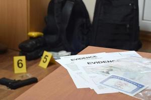 las etiquetas de evidencia y la tarjeta verde con el número ssn se encuentran en la mesa con una gran cantidad de elementos como evidencia en el proceso de investigación de la escena del crimen en el fondo foto