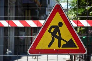 The warning sign under construction is attached to a metal mesh fence with a red and white striped signal tape photo