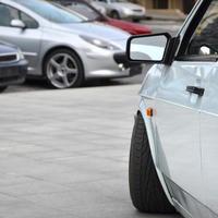 Diagonal view of a white glossy car that stands on a square of gray tiles photo