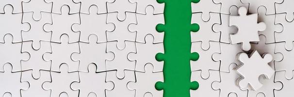 The green path is laid on the platform of a white folded jigsaw puzzle. The missing elements of the puzzle are stacked nearby. Texture image with space for text photo