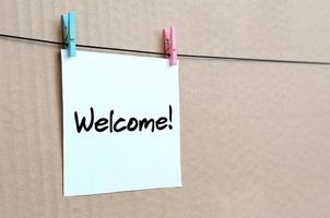 Welcome Note is written on a white sticker that hangs with a clothespin on a rope on a background of brown cardboard photo