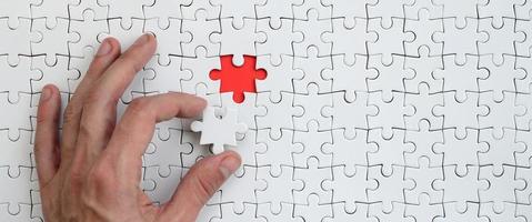 The texture of a white puzzle puzzle in the assembled state with one missing element that the male hand puts in photo