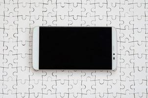 A modern big smartphone with a touch screen lies on a white jigsaw puzzle in an assembled state photo