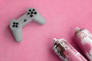 Teenagers and youth lifestyle concept. Joystick and two spray cans lies on the blanket of furry pink fleece fabric. Controllers for video games and paint cans on a plush fleece material background photo