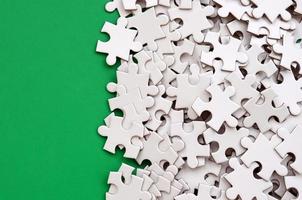 A pile of uncombed elements of a white jigsaw puzzle lies on the background of a green surface. Texture photo with copy space for text
