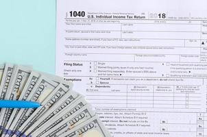 1040 tax form lies near hundred dollar bills and blue pen on a light blue background. US Individual income tax return photo