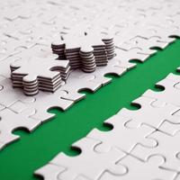 The green path is laid on the platform of a white folded jigsaw puzzle. The missing elements of the puzzle are stacked nearby. Texture image with space for text photo